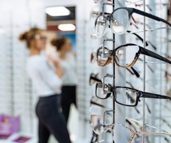 Stand with glasses in the store of optics. Woman chooses glasses.